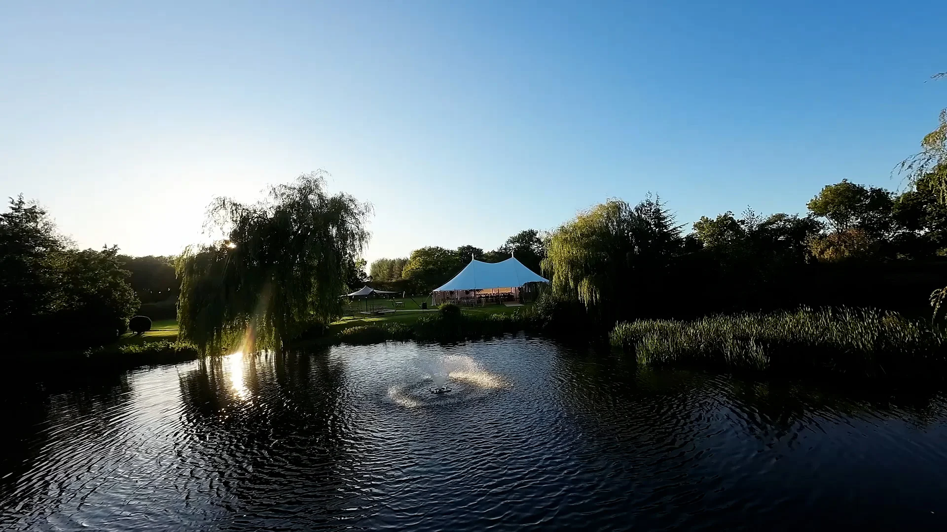 White marquee beside a lake at sunset